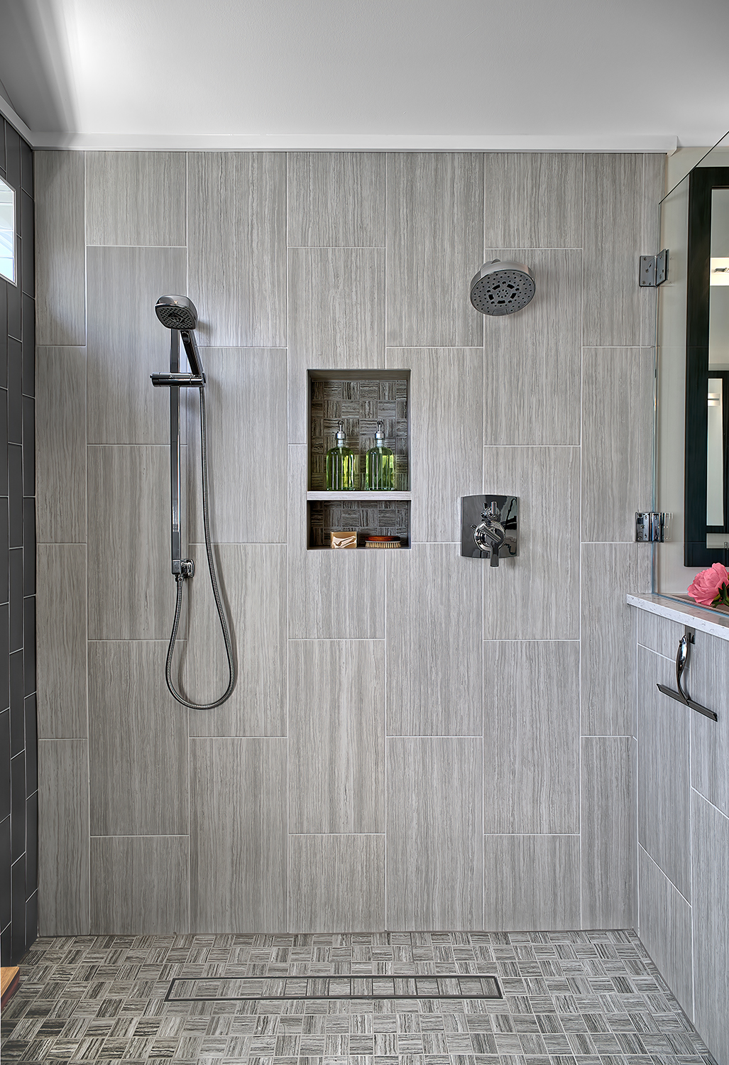 Shower with handheld and standard shower heads. Floor has horizontal drain.